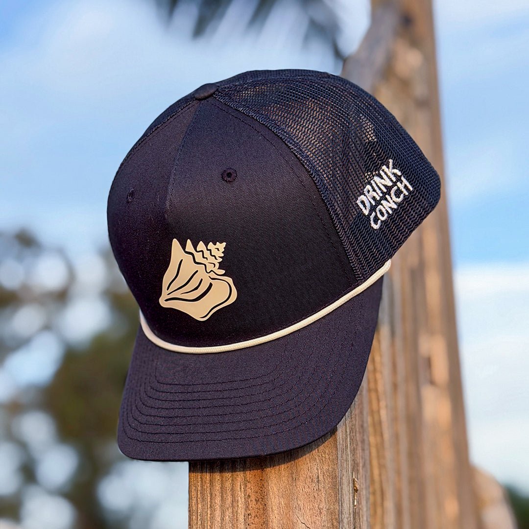 Drink Conch trucker hat sitting on wooden post